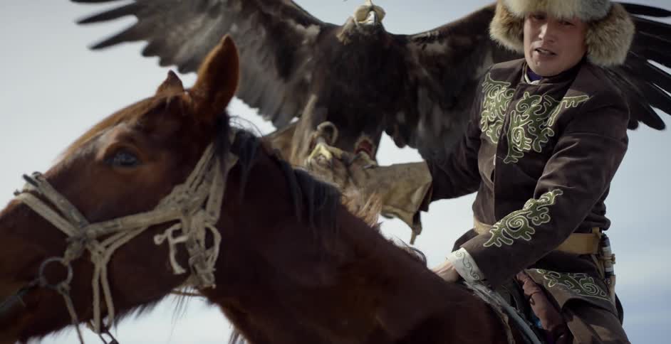 A man mounts a horse with a hunting eagle