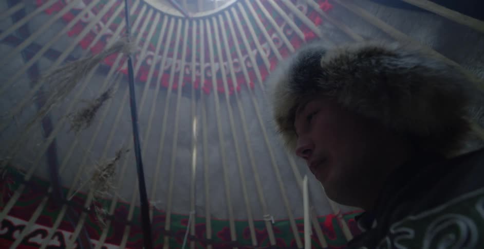 A mongolian man is standing inside a yurt during the day