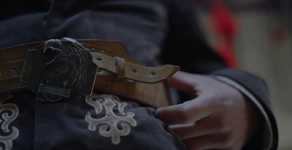 A person wears a leather belt with an ornate eagle buckle