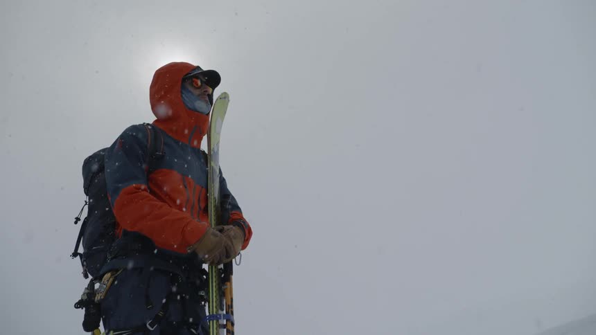 A person is standing as it snows holding skis