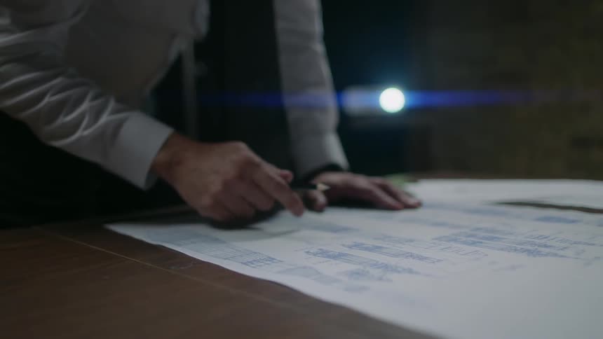A man holding a pen leans over a table looking at a plan