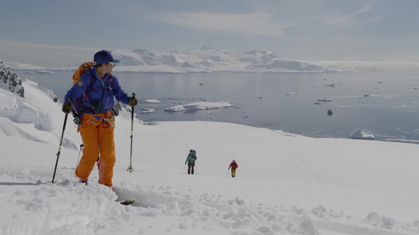 Group of people hike up a snowy mountain using poles and a rope