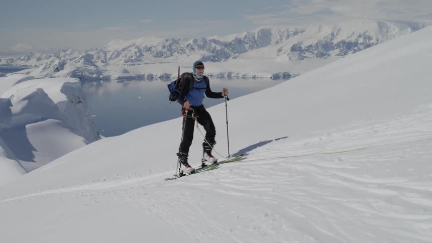 Person hikes up a snowy mountain wearing skis and using ski poles