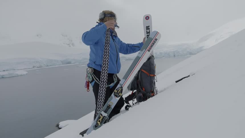 A man standing on a slope puts skuff saver tape on a ski