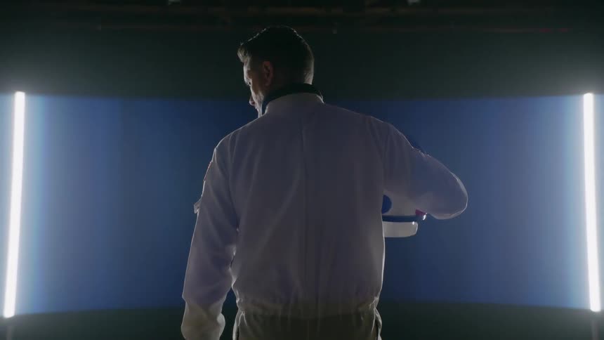 An astronaut stands in front of a line of lights