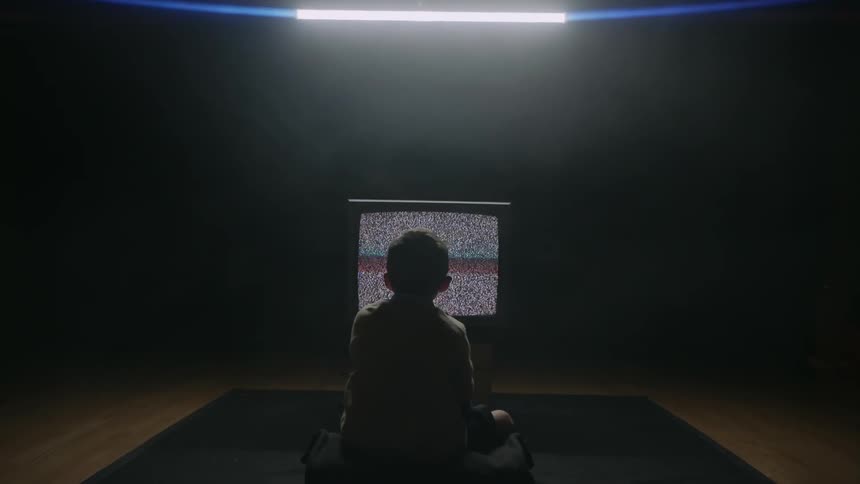 A boy sits in front of a television showing static