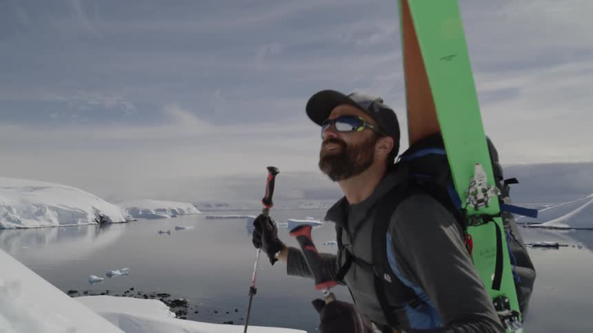 A man carrying his skis uses poles to help climb a steep slope
