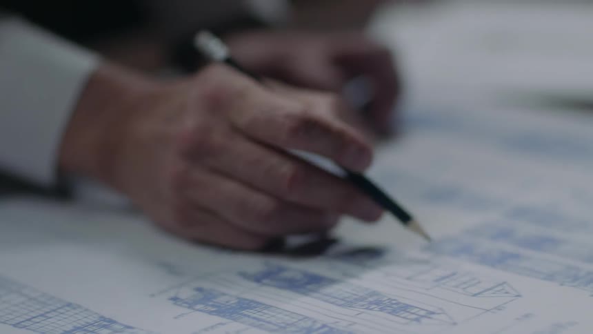 A person holding a pencil looks at a plan on a desk