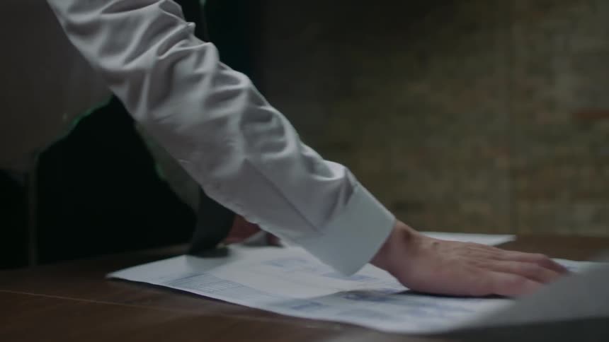 Man unrolls a sheet of paper onto a table