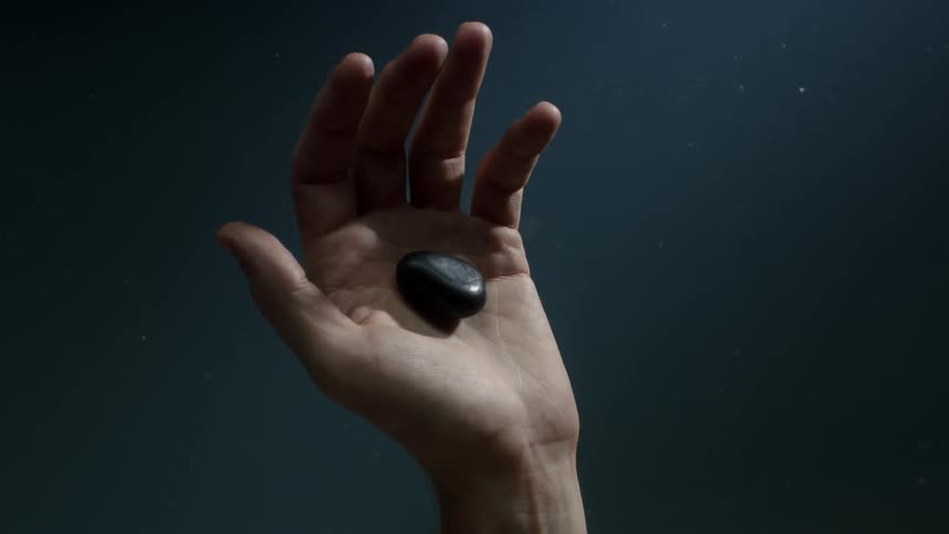 Hand showing and then releasing a black rock into some water below