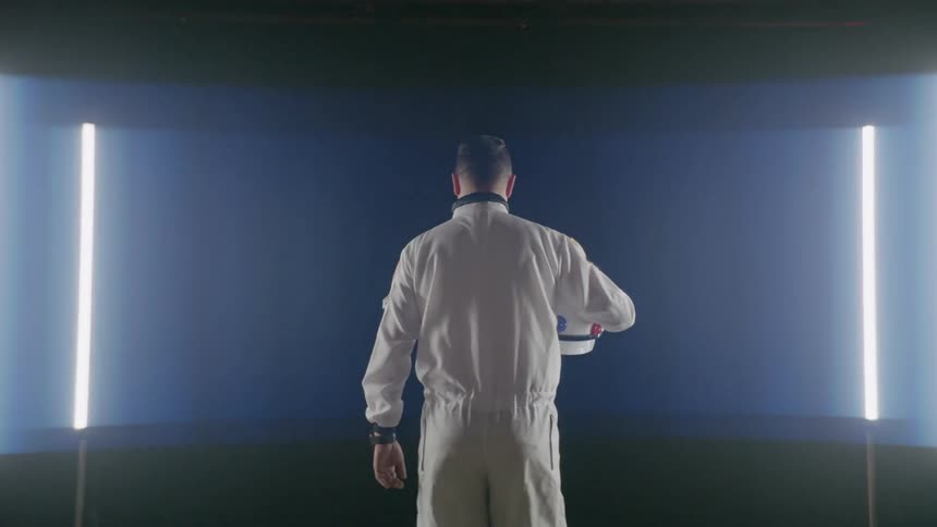 Man wearing a white suit holding a white helmet looks at a large curving screen