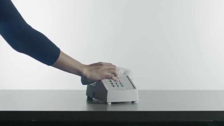 Person pushes buttons on a landline phone on a desk