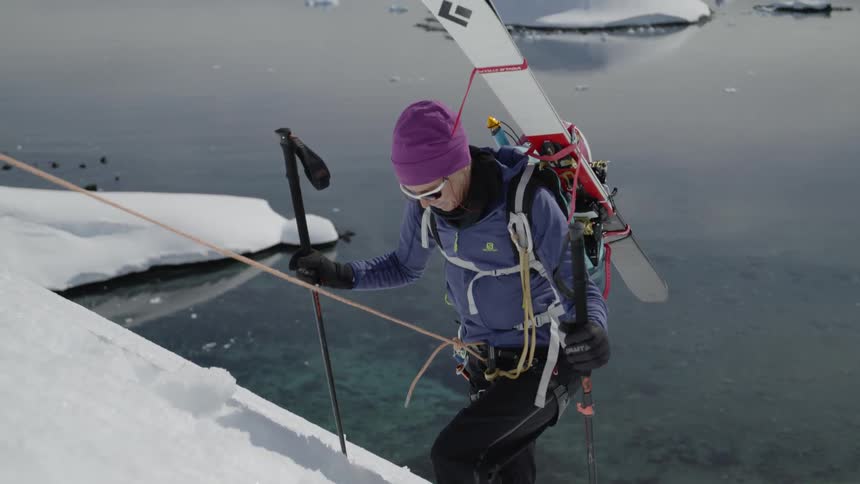 A woman presses her poles into the snow as she climbs a mountain