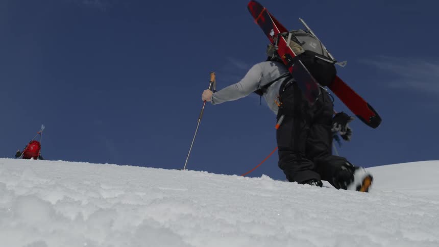 Two people use poles and a rope to hike up a snowy mountain