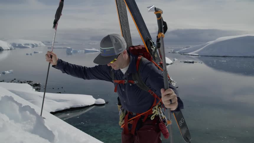 A man hikes up a mountain  with skis on a beautiful day in Antarctica