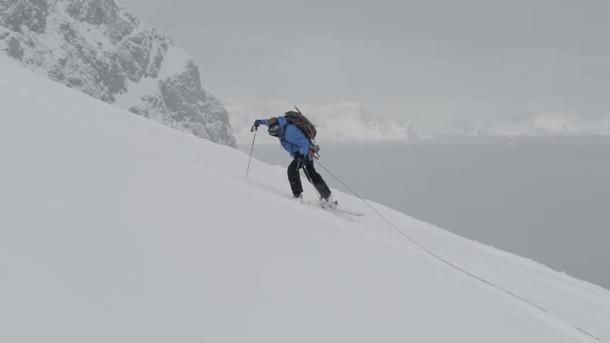 Person wearing skis hikes up a mountain using a rope and ski poles