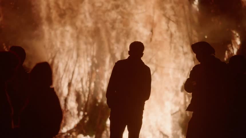 People walking near a blazing fire outside at night