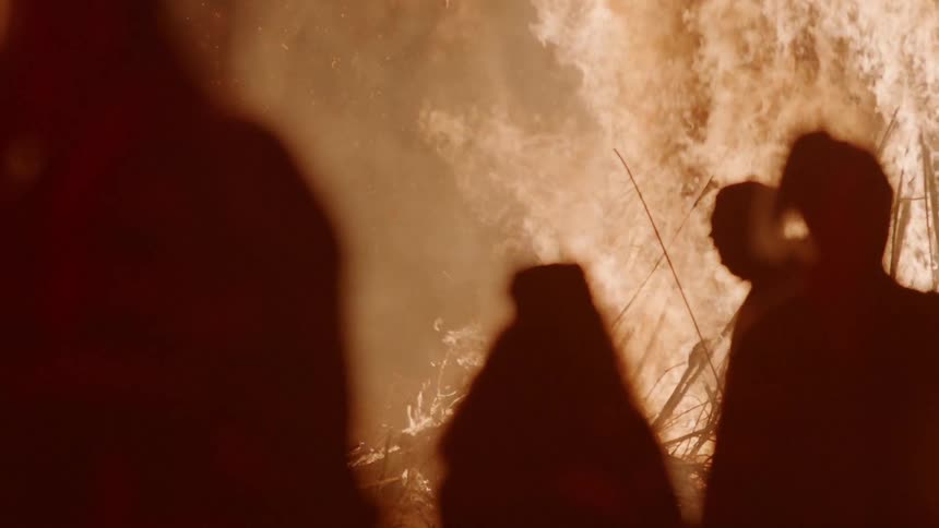 A huge fire is blazing as people walk past at night