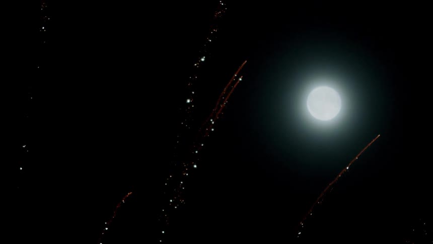 Moon shines brightly as fireworks fly towards the night sky