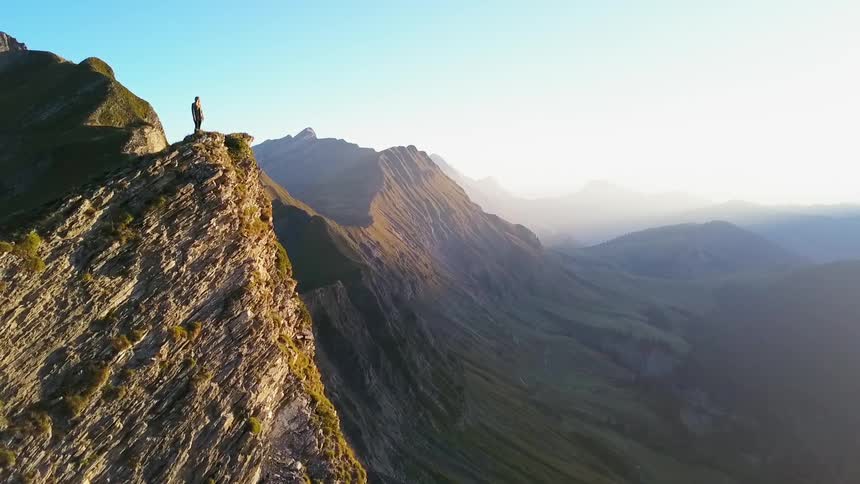A man stands on top of the tall mountain looking at the skyline