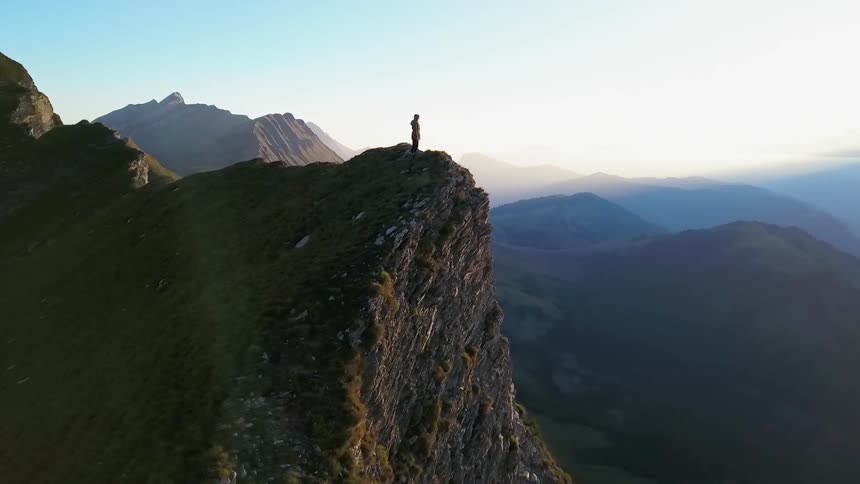 A person stands on the edge of a steep mountain cliff