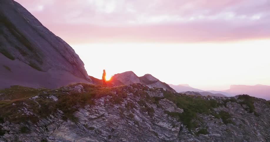 A person standing on top of the mountain begins walking as the sun sets