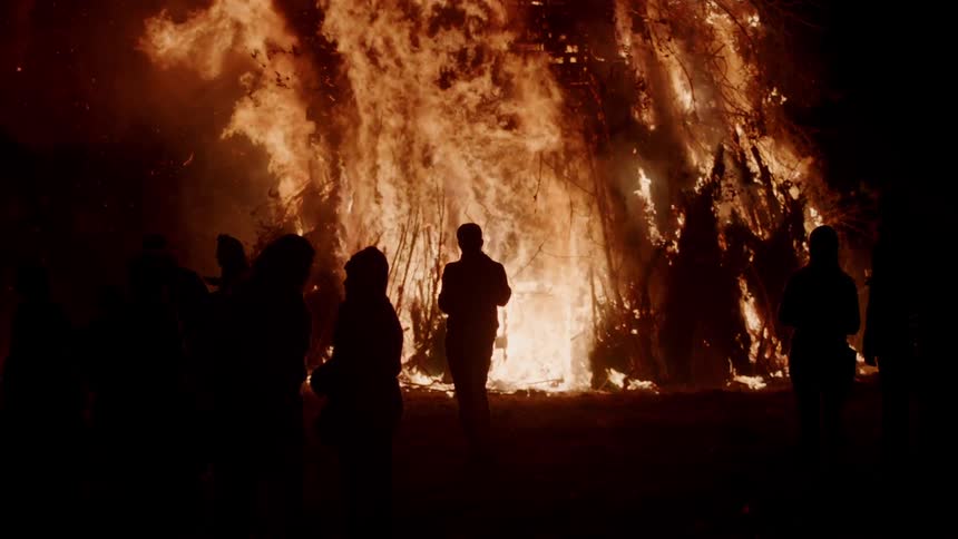 People watch a large fire burn at night