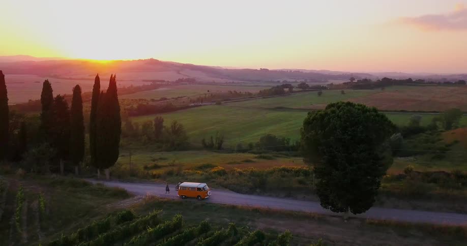 People walk over to an orange bus on the road