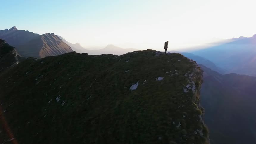 A hiker stands on a mountain peak at sunset