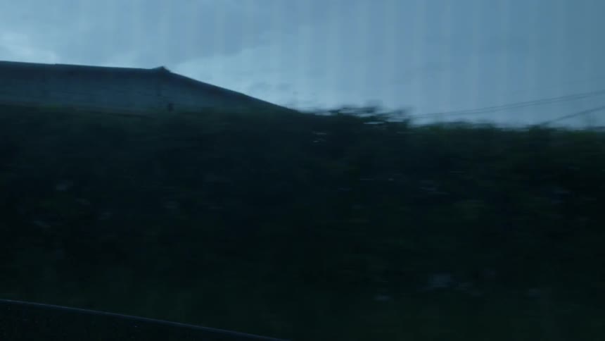 A vehicle drives on a rural road in the rain