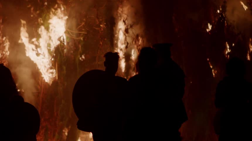 People watch a fire blazing brightly outside at night
