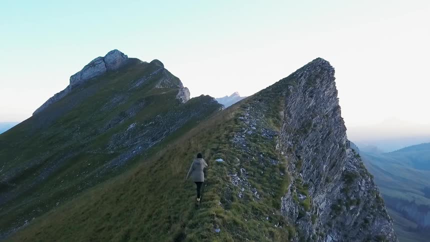 A woman is hiking a mountain ridge to a peak during the day