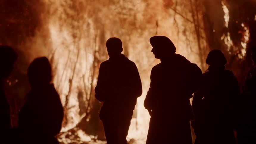 A group of people stand by a burning bonfire