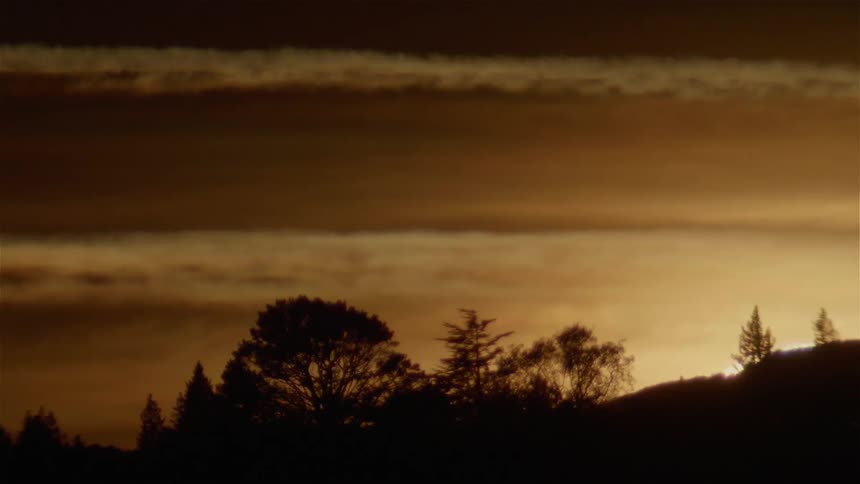 The sun is setting behind a hillside on a cloudy day