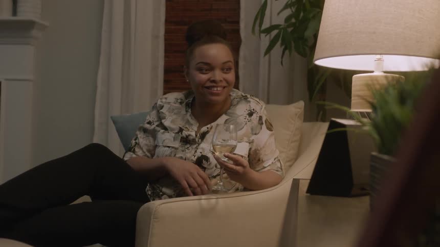 Woman holding a glass of wine sits in a chair and waves and talks