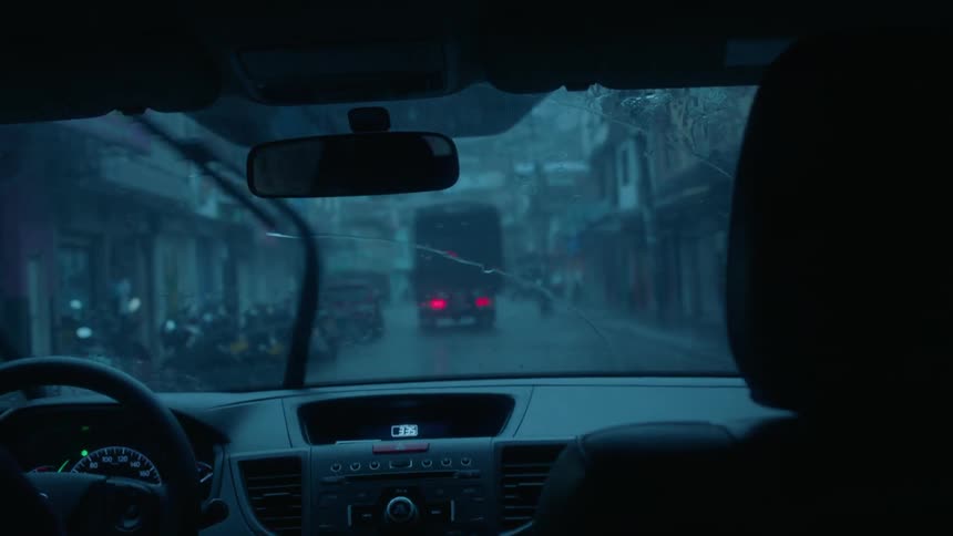 A car is driving down the rainy street behind a truck