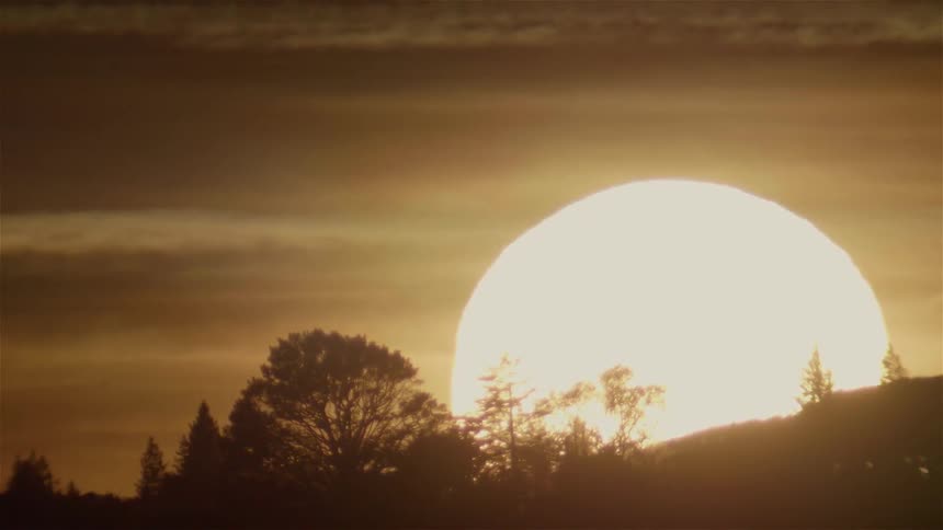 The sun is setting behind a hillside on a cloudy day
