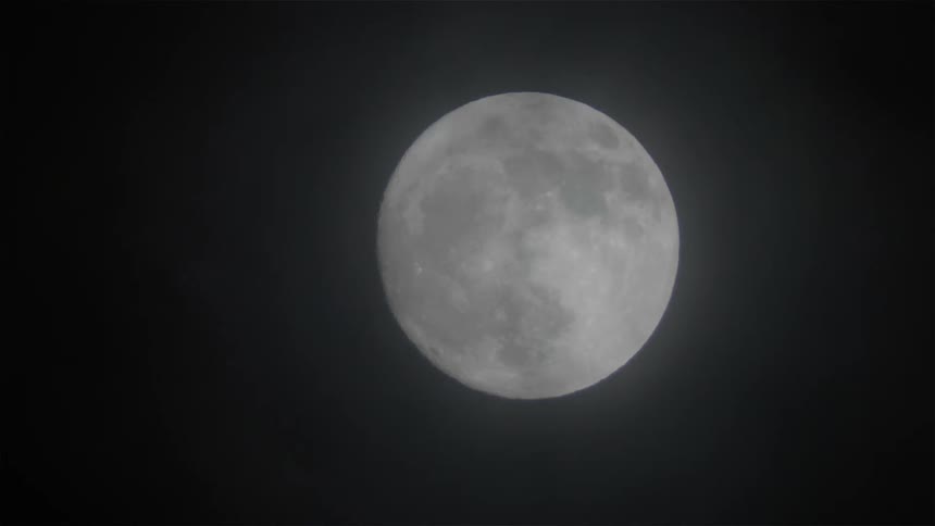 Full moon sitting against a dark sky as light clouds pass in front