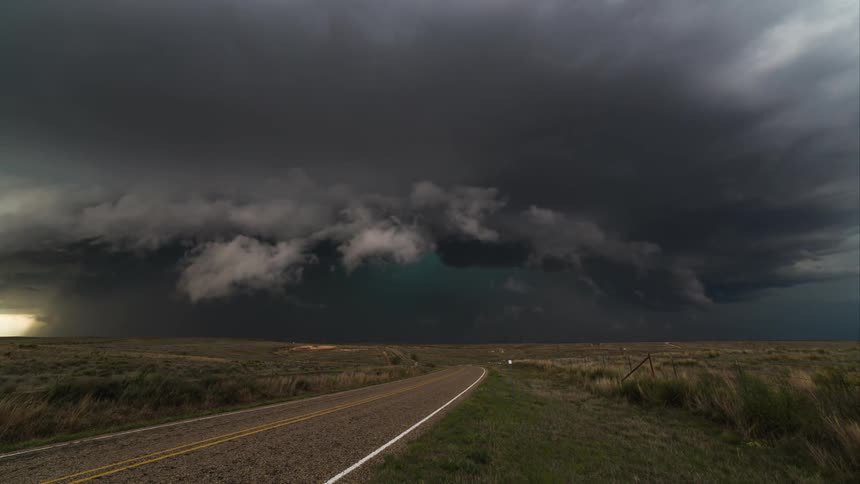 Dark storm clouds gather over a road in a rural area