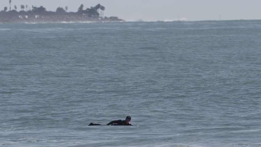 A person floating on a board in the ocean, slowly paddles with their arms