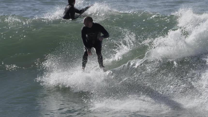 Surfers in the water as one catches a wave and rides it towards shore