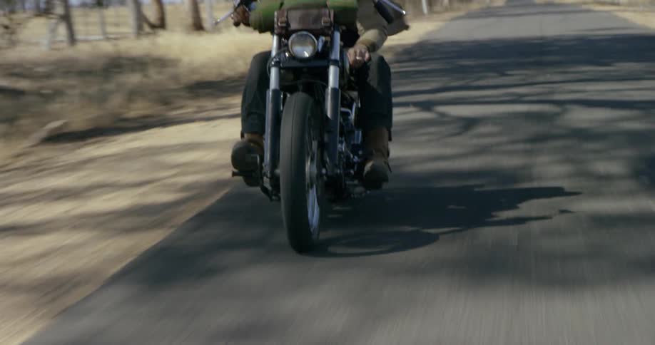 Man rides a motorcycle on a tree lined country road