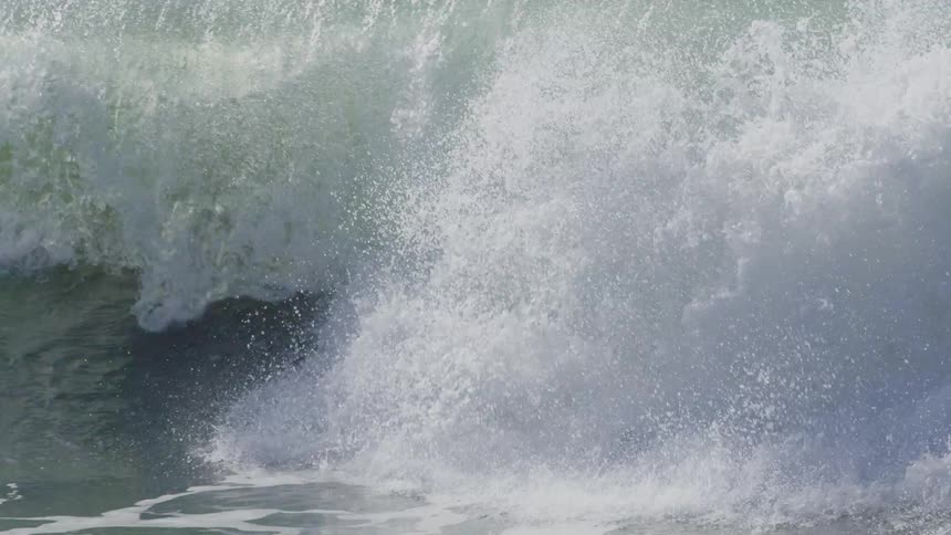 Waves slash down as a person swims behind