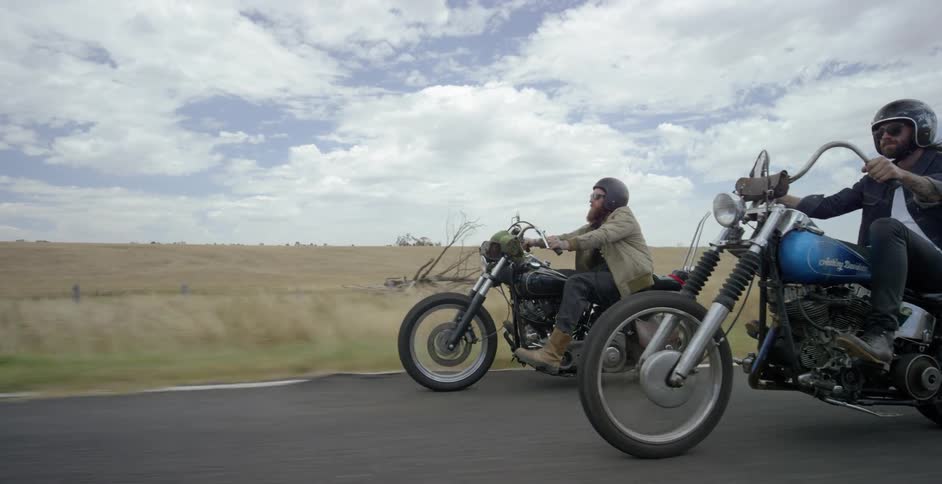 Two men are riding motorcycles on a rural road on a cloudy day