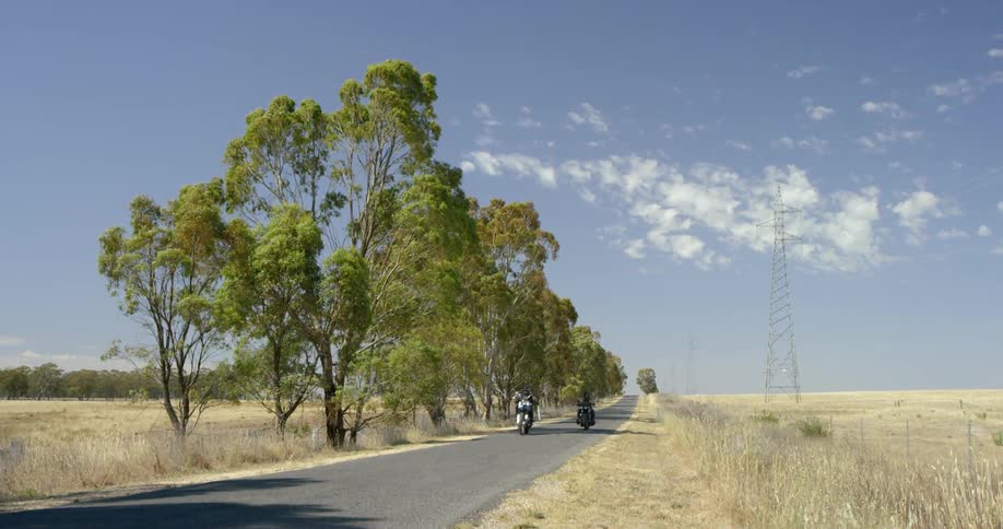 Two men are riding motorcycles on a rural road on a windy day