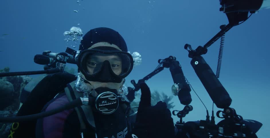 Underwater diver surrounded by equipment blows out bubbles and gives a thumbs up