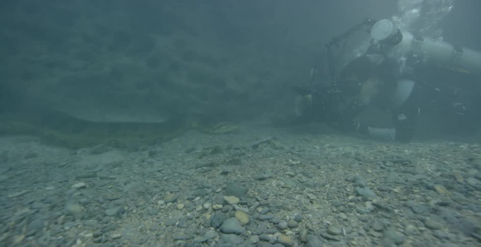 The diver is on the rocks in the deeper part of the water filming