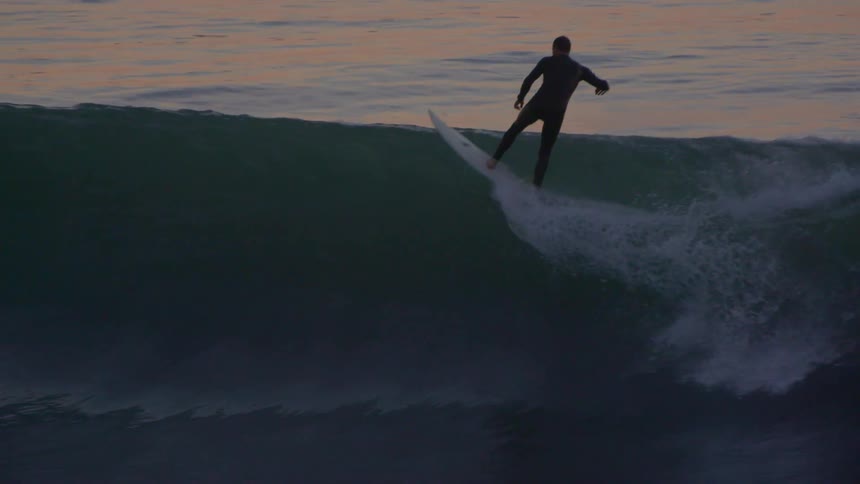 A person in a full body wetsuit rides the waves on a surfboard