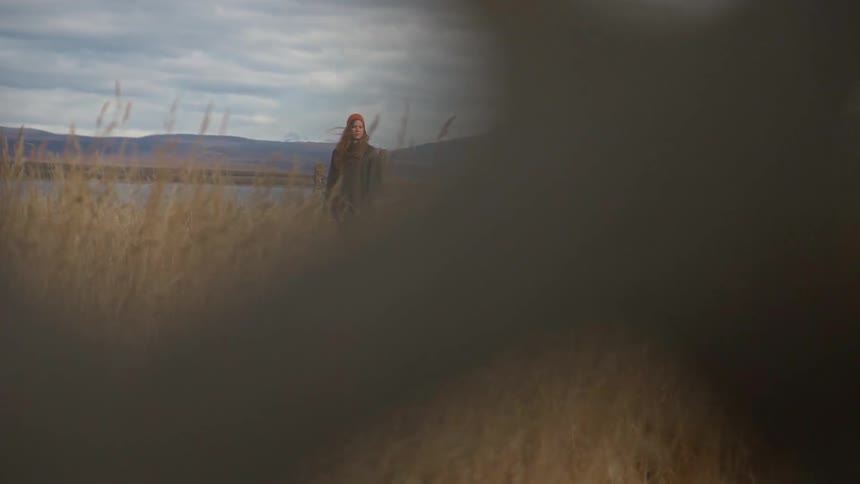 A woman stands on the field by the lake