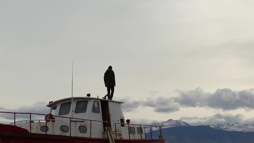 A man walks on the roof of a boat's cabin
